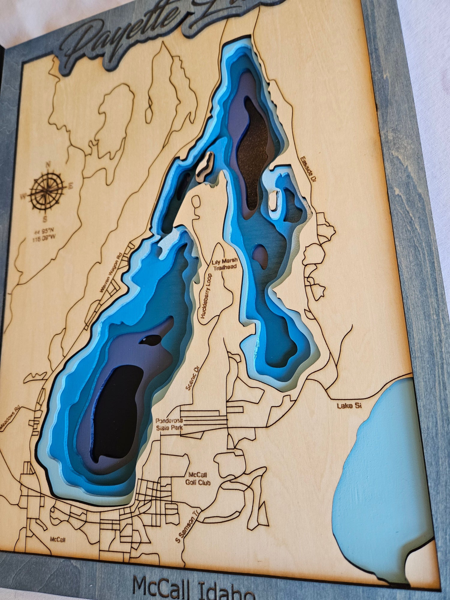 Wooden map with laser-cut topography of a lake, featuring blue for water and brown for land.