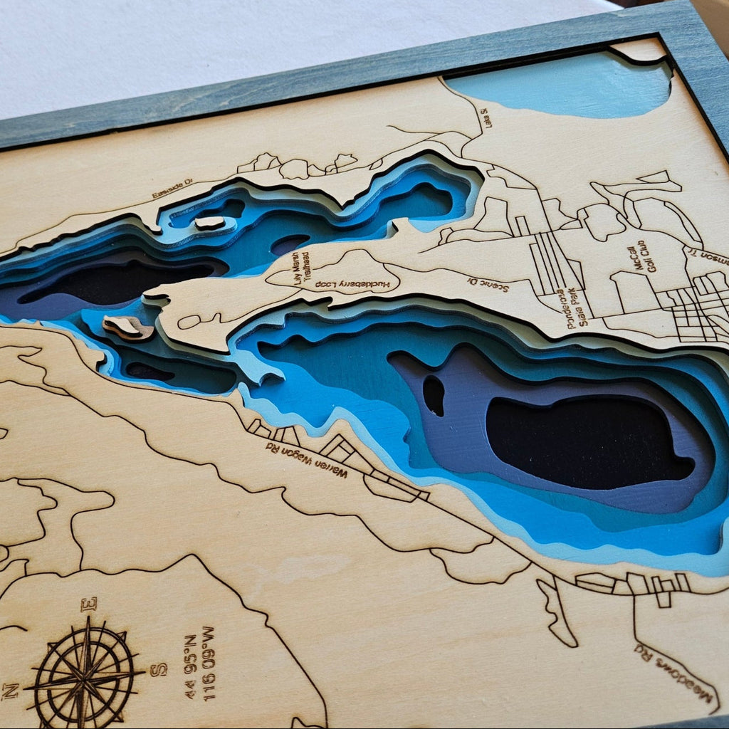 Wooden topographic map of a lake with cut-out water feature, displayed on a chair.