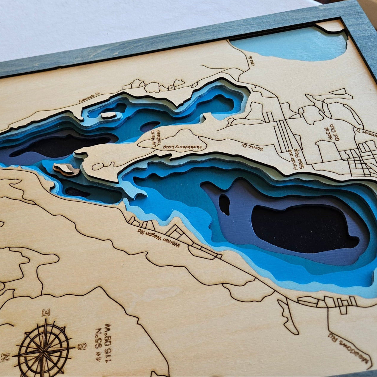 Wooden topographic map of a lake with cut-out water feature, displayed on a chair.