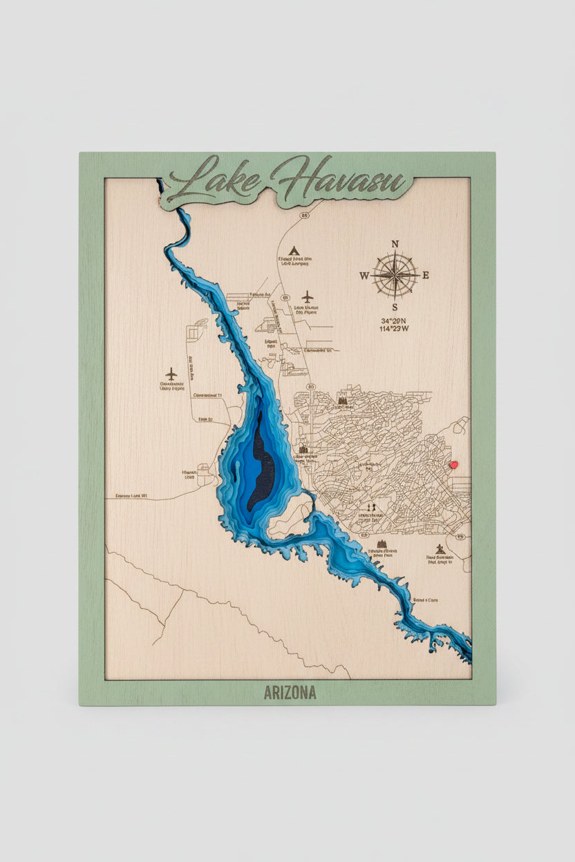 A framed wooden Lake Havasu map print with a light natural wood background, blue water channels, a green border, and a raised script title reading 'Lake Havasu' at the top, displayed on a wooden surface.