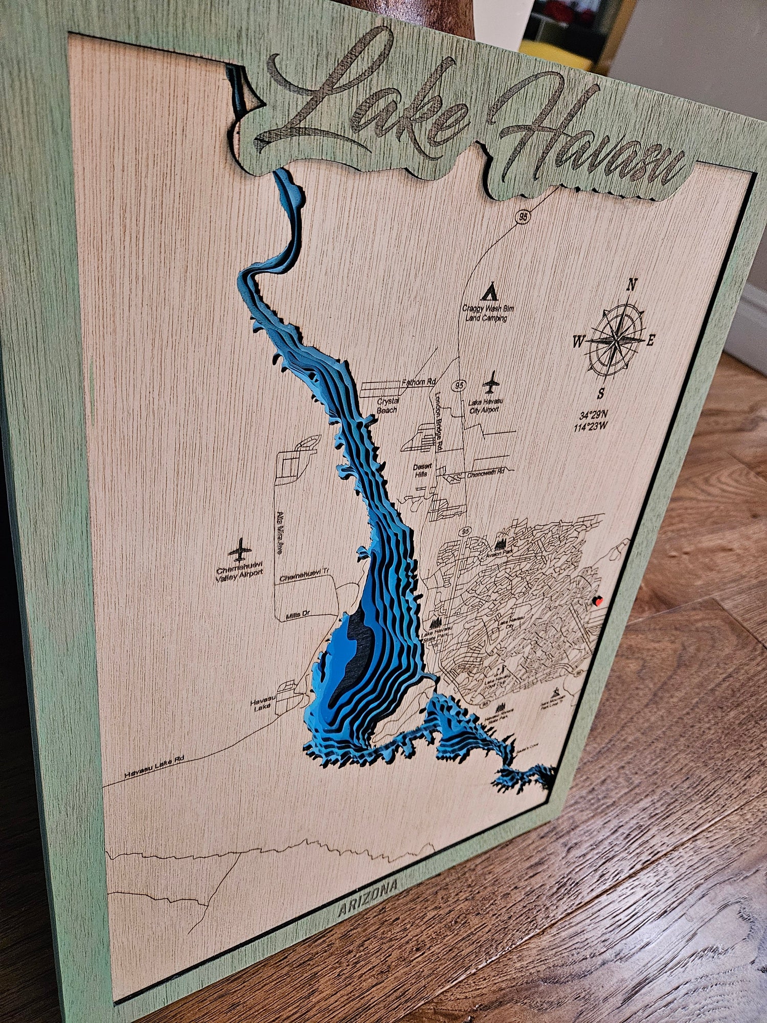 A 3D laser-etched wooden map of Lake Hawaii, featuring a light natural wood background, a green border, and a raised blue contour design representing the lake. The top is personalized with 'Lake Hawaii' in script, and a compass rose is shown on the right.