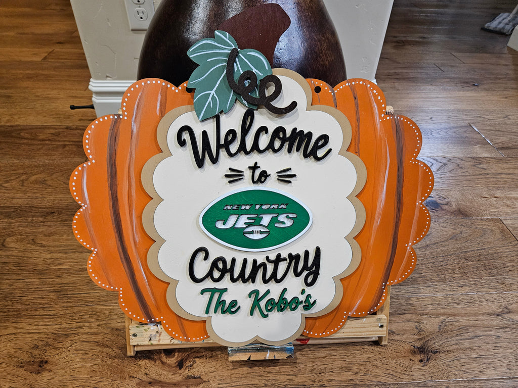 A decorative New York Jets themed sign shaped like a scalloped orange pumpkin with a white center panel reading 'Welcome to Country The KoBo's' and featuring the Jets logo.