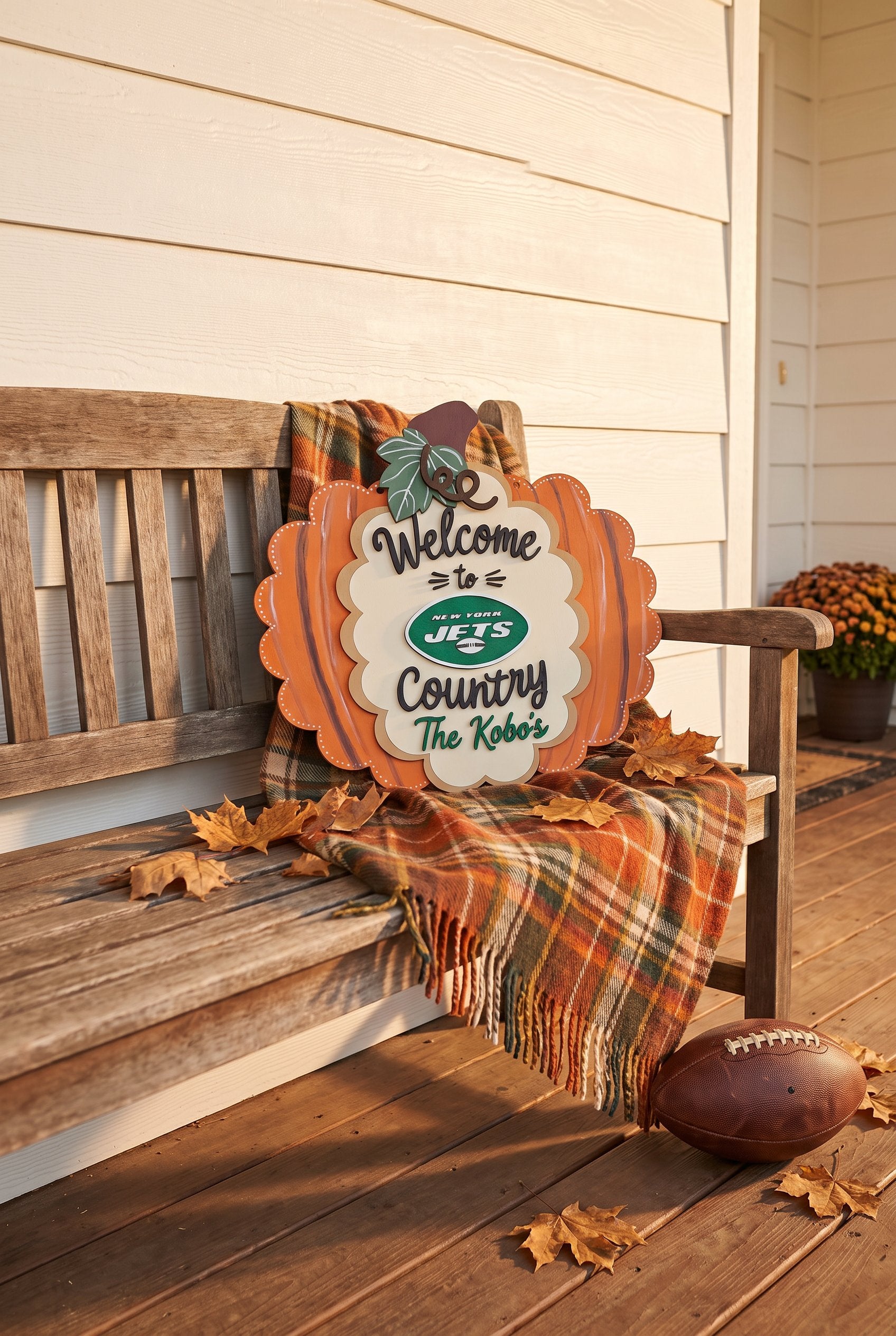 A decorative autumn sign shaped like a pumpkin sits on a wooden porch bench. The sign reads “Welcome to Jets Country The Ko’b’s” with the New York Jets logo in the center.