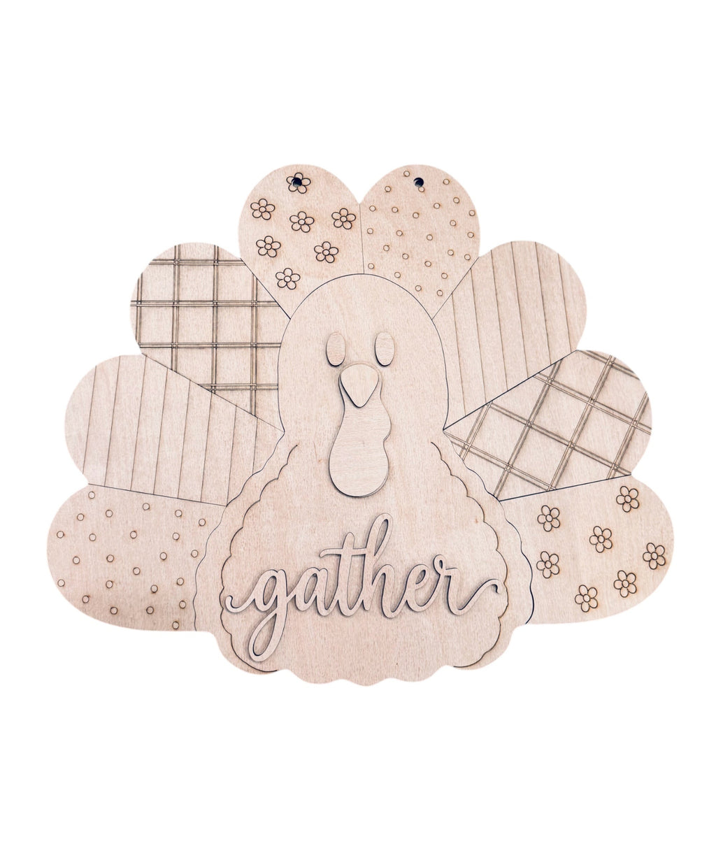 A wooden Thanksgiving decorative sign shaped like a turkey, featuring engraved patterns on the feathers and the word 'gather' in script on the body, shown on a plain white background.