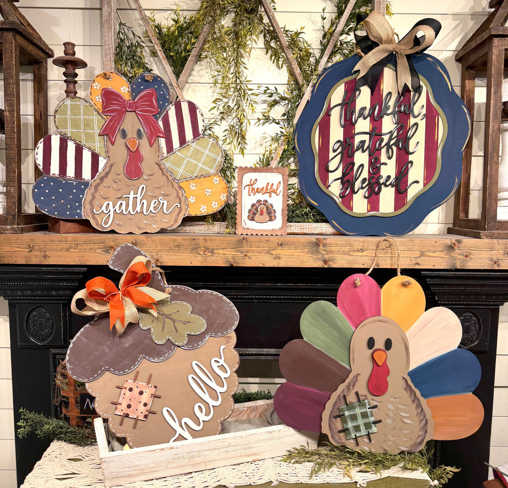 A collection of rustic, hand-painted wooden Thanksgiving-themed signs displayed on a wooden mantel. The set includes a multi-colored turkey sign with 'gather' written on its belly, a round sign with 'thankful grateful blessed' script, a brown turkey sign with 'hello' in white script, and a small square 'Thankful' card, all styled against a black fireplace.